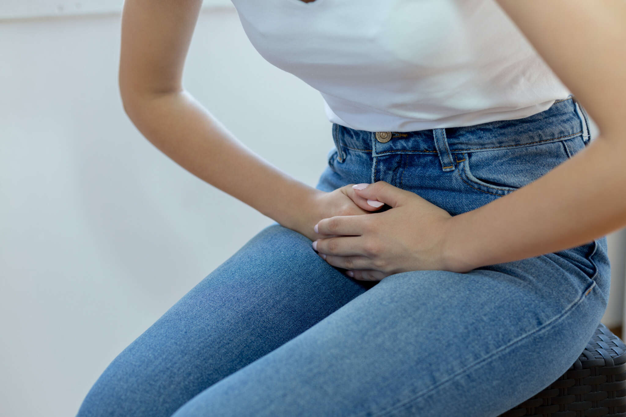 Person in Jeans und weißem T Shirt hält sich die Blase