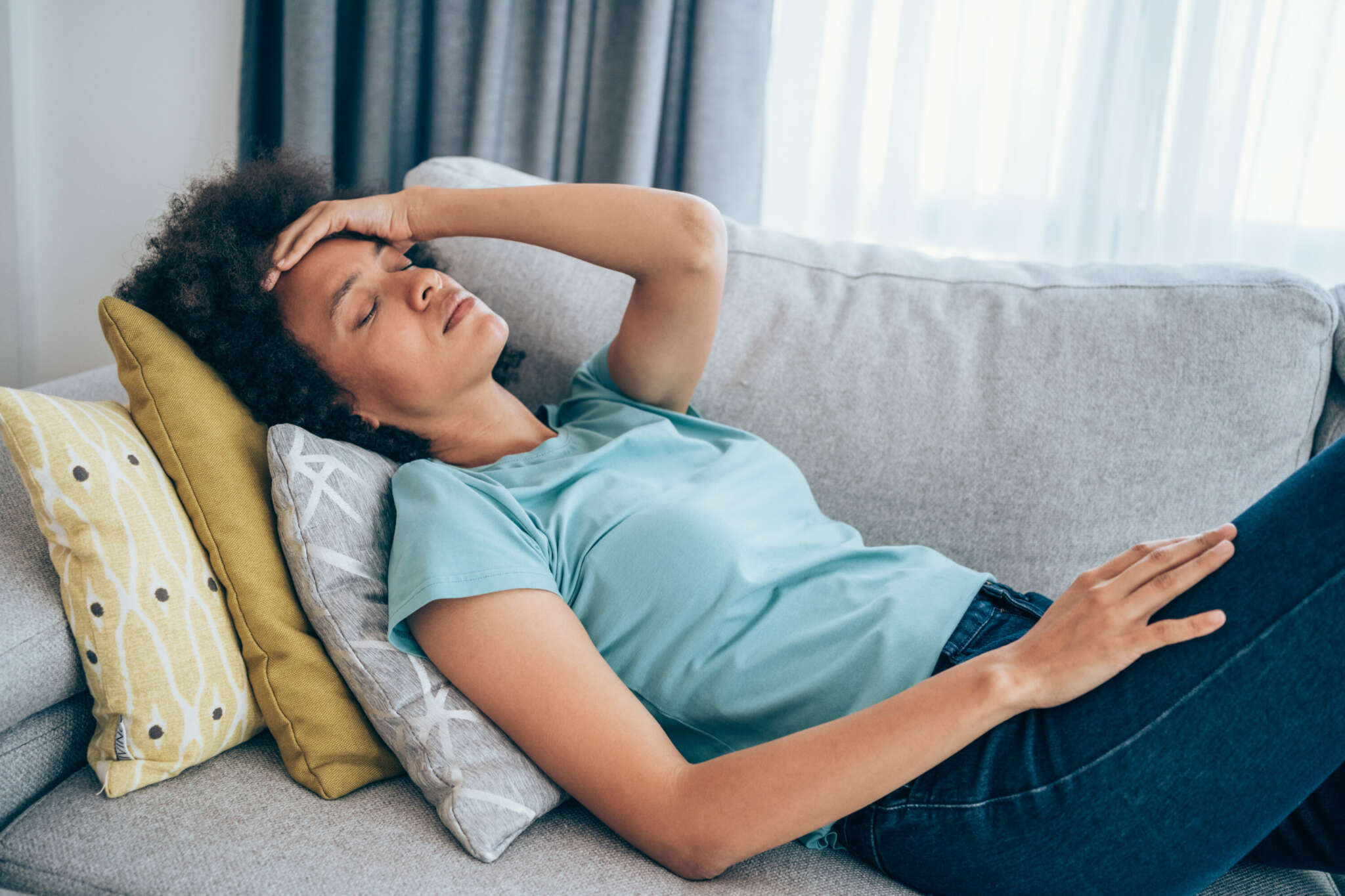 Liegende Frau auf Sofa mit Kissen im Nacken und Hand auf der Stirn