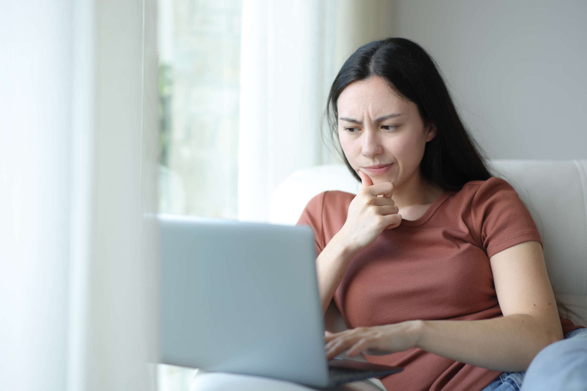 Frau schaut skeptisch auf den Bildschirm ihres Laptops