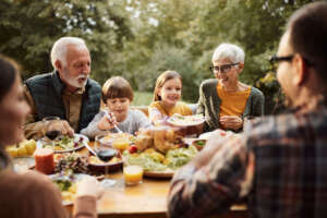 Eine Familie mit Großeltern, Eltern und Enkeln sitzt an einem gedeckten Abendbrottisch im Garten und unterhält sich gut gelaunt
