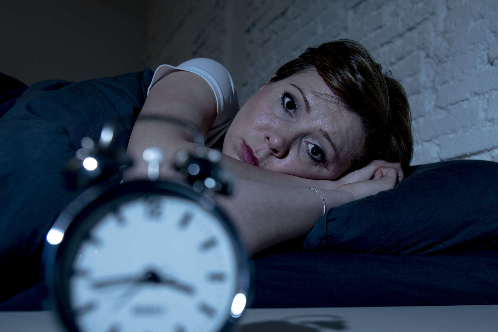 Frau liegt wach im Bett, im Vordergrund ist ein Wecker zu sehen