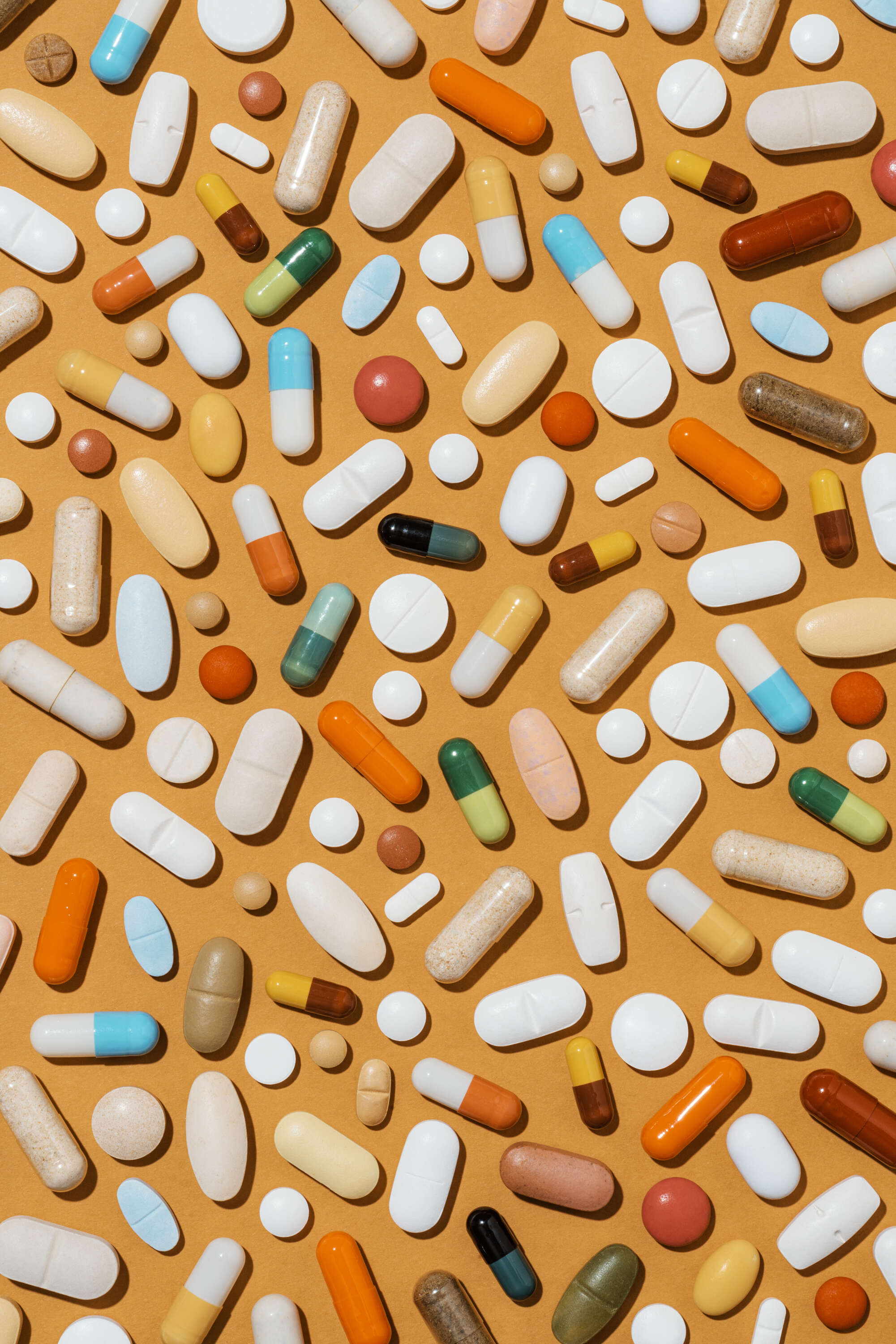 Bunte Tabletten und Medikamente auf orangefarbenem Hintergrund.