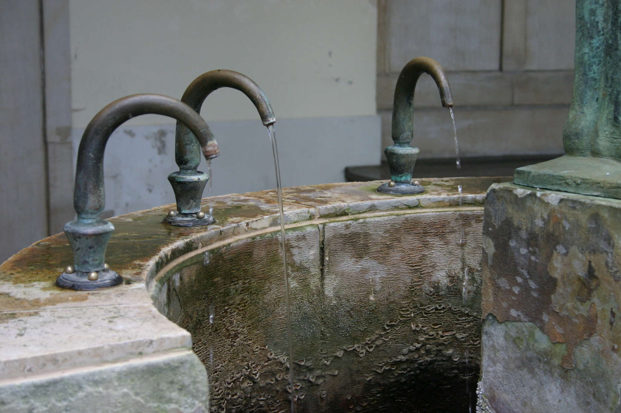 Mehrere Wasserhähne an einem alten Trinkbrunnen, aus denen Wasser fließt.